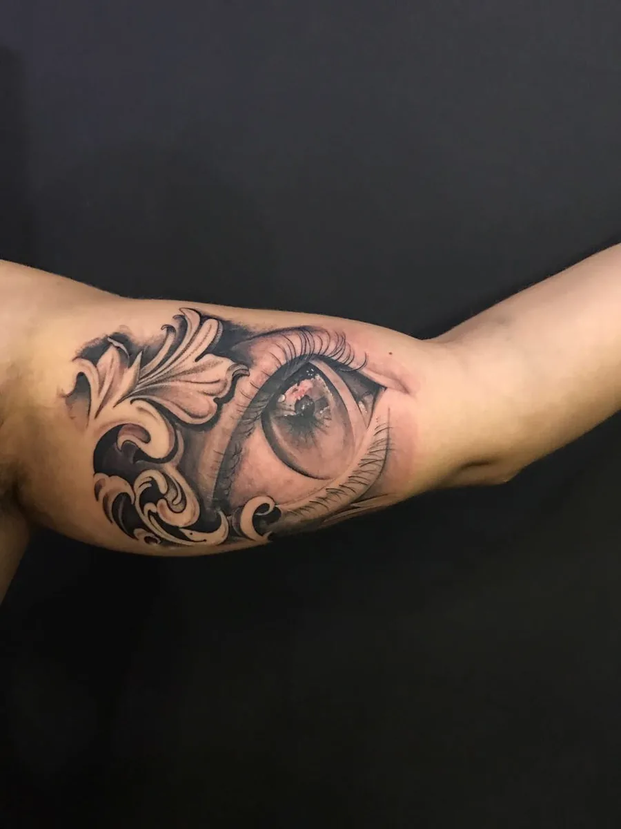 Olho realista com ornamentos florais no bíceps
